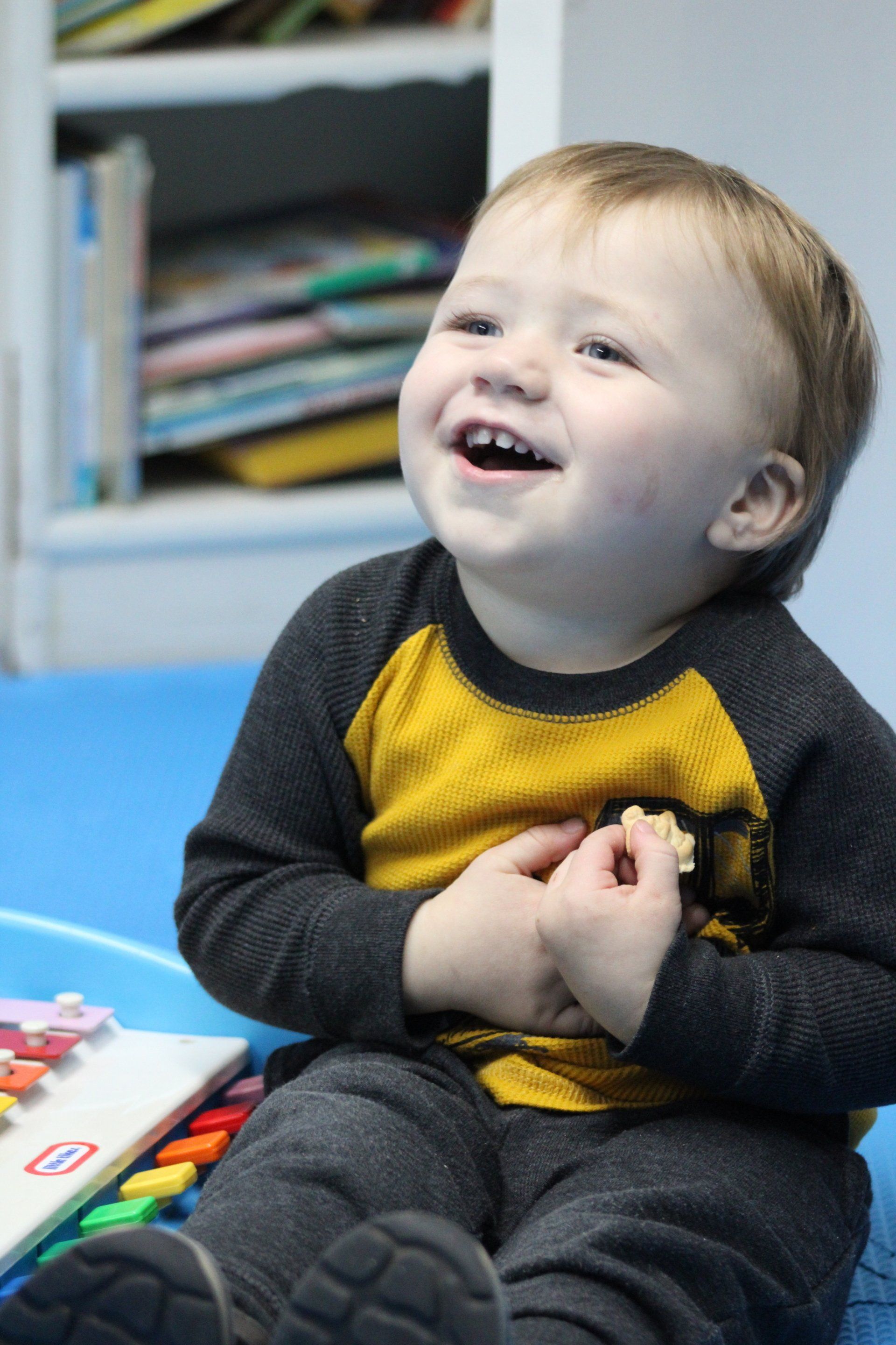 A baby in a yellow and gray shirt is smiling