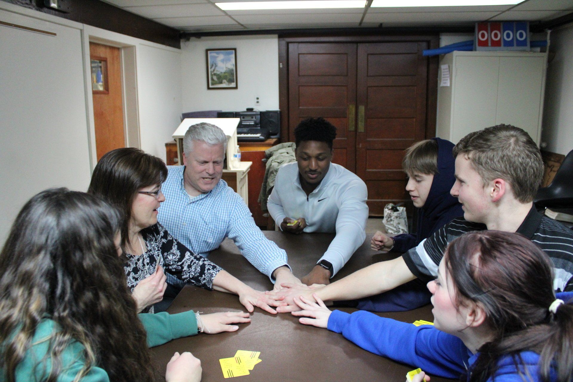A group of people are sitting around a table putting their hands together.