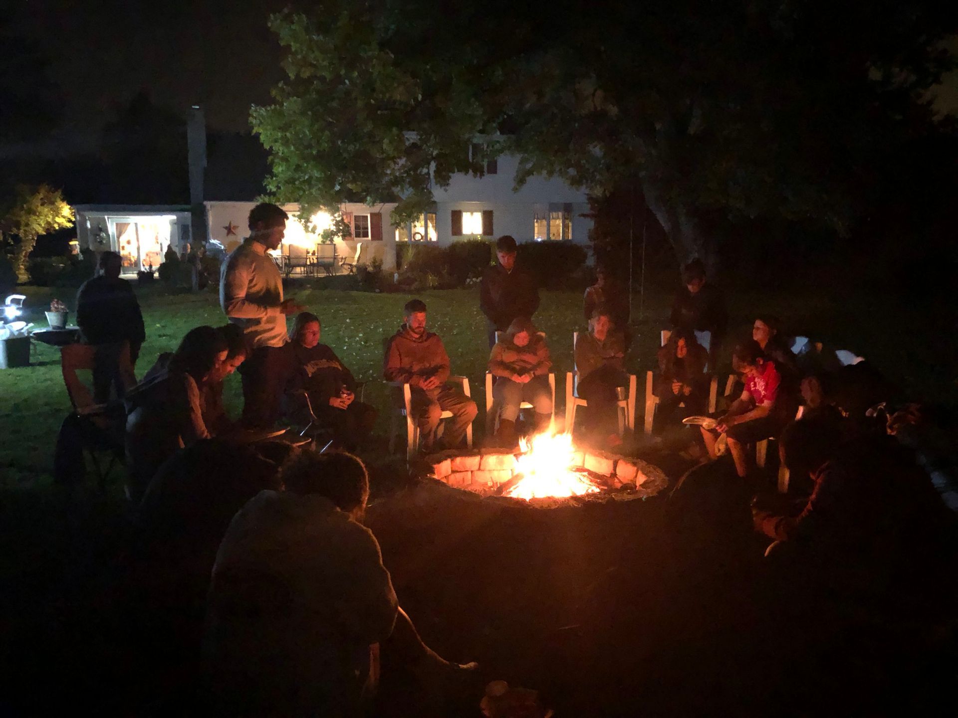 A group of people are sitting around a fire pit at night.