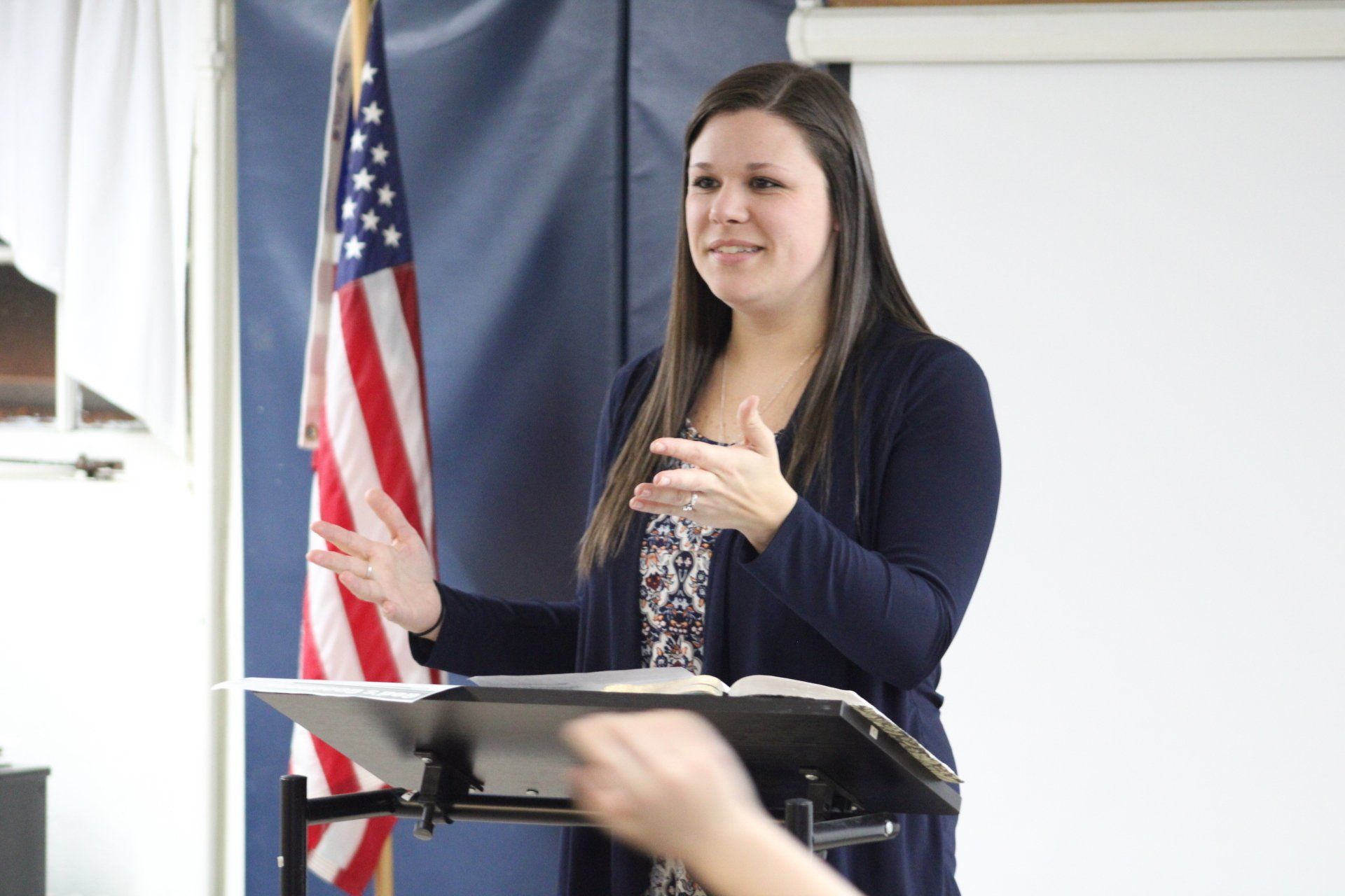 A woman is giving a speech at a podium in front of an american flag.