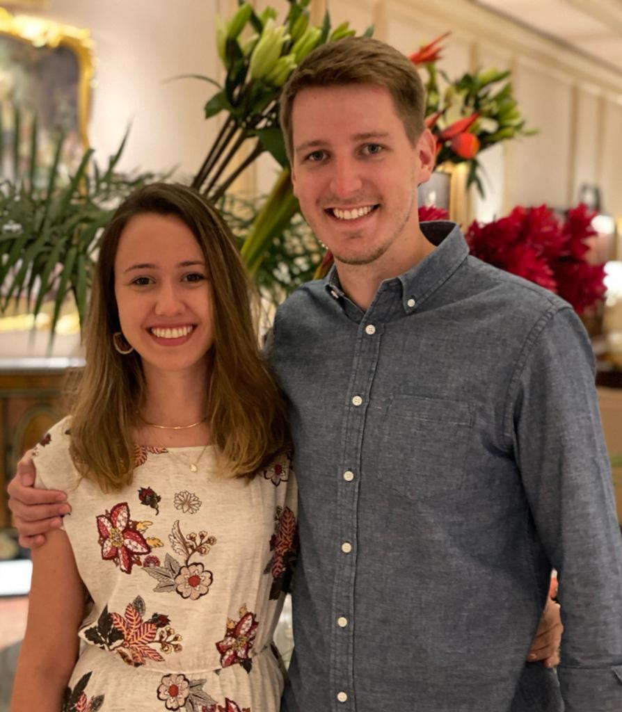 A man and a woman are posing for a picture in front of flowers.