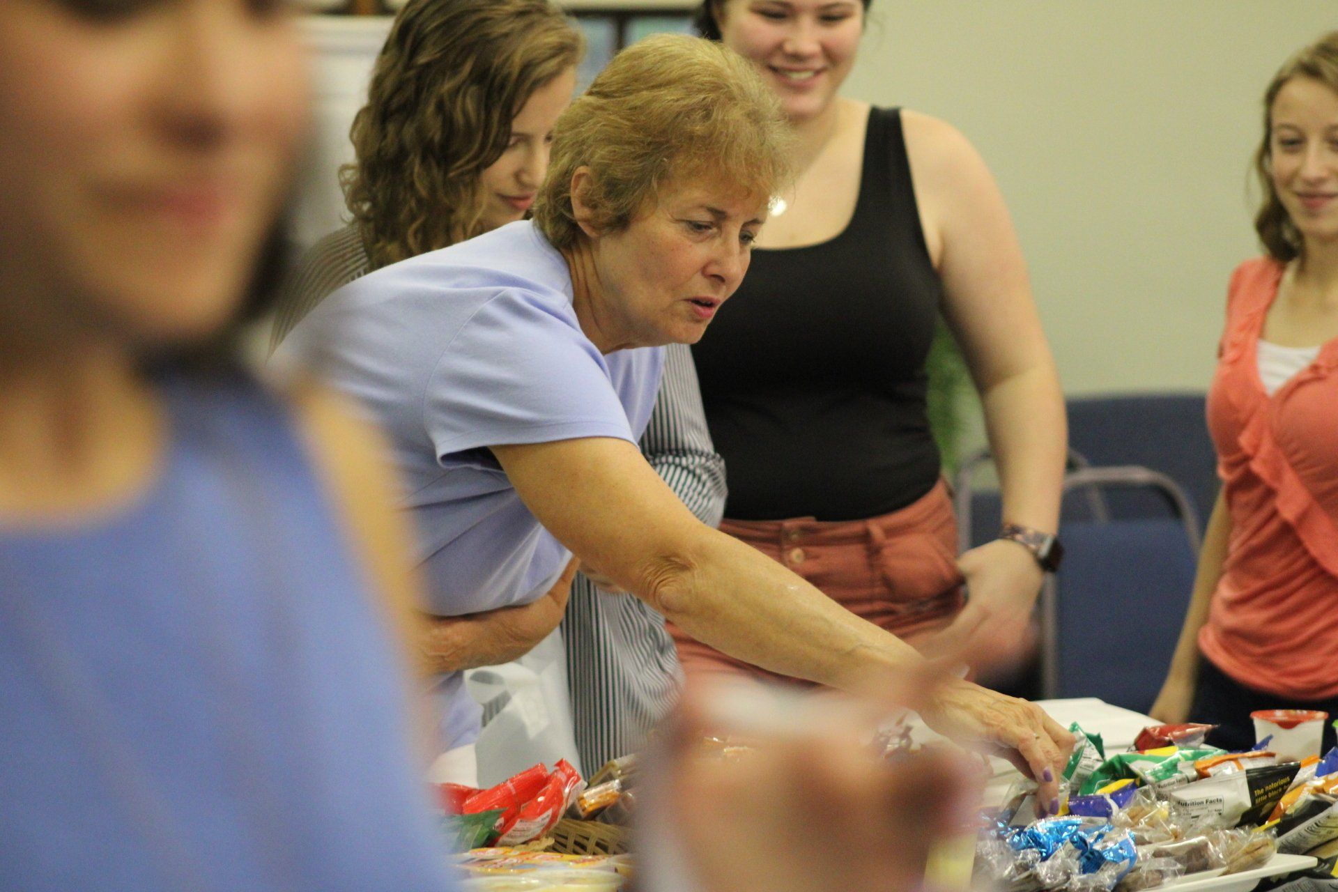 A group of women are standing around a table looking at candy.