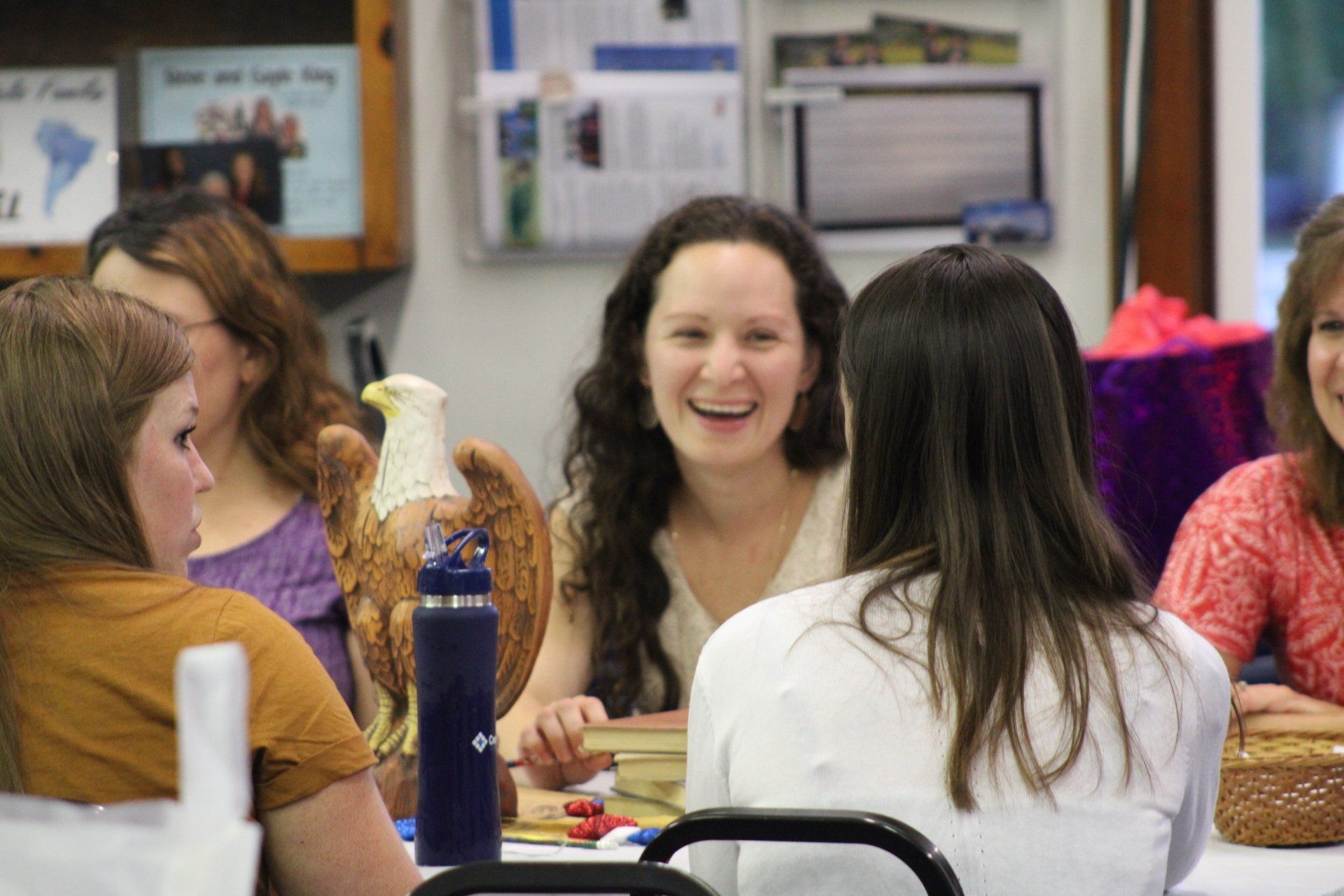A group of women are sitting at a table with a statue of an eagle.