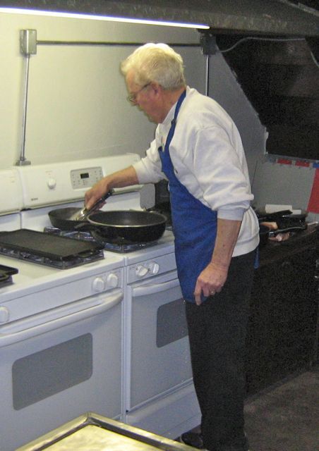 A man in a blue apron is cooking on a white stove