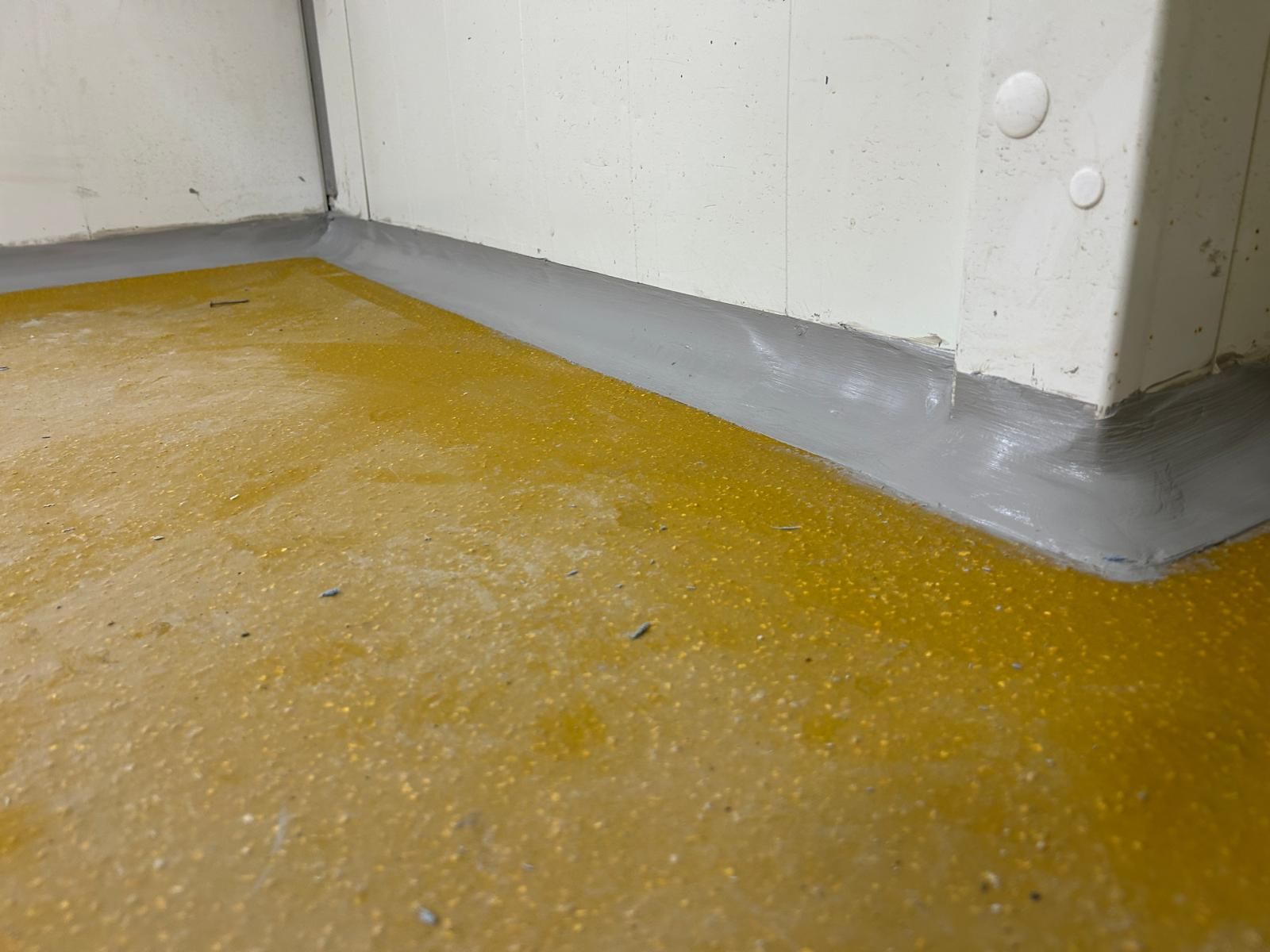 Pavimento del magazzino con attraversamento pedonale dipinto di arancione e segnaletica orizzontale su superfici bianche e verdi.