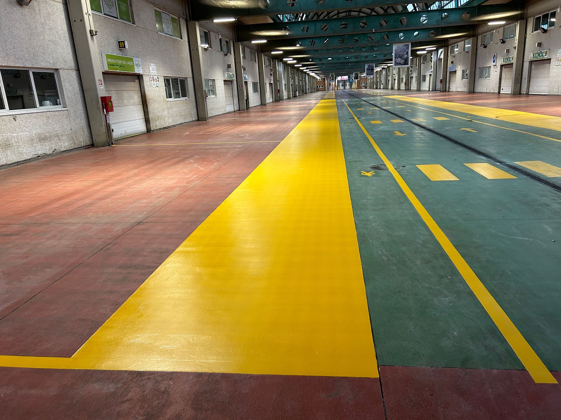 Pavimento del magazzino con attraversamento pedonale dipinto di arancione e segnaletica orizzontale su superfici bianche e verdi.