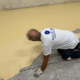 Un uomo è inginocchiato e sta applicando del sigillante giallo su un pavimento di cemento.