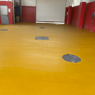 Pavimento giallo in un garage con diversi tombini. Sono visibili anche pareti rosse e una grande porta bianca.
