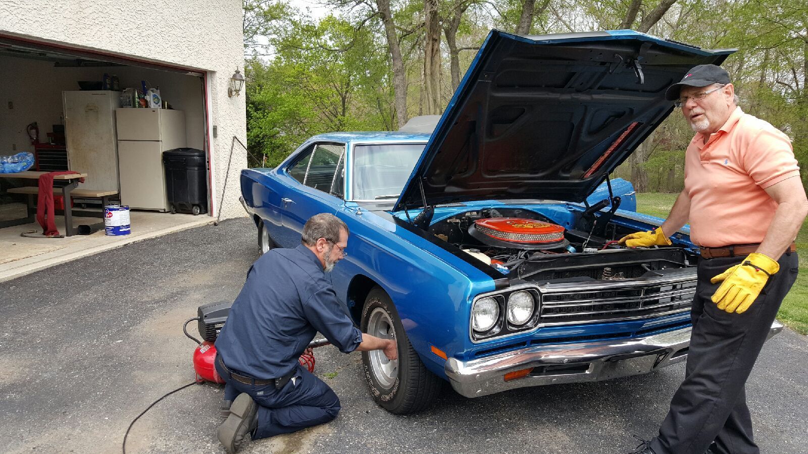 Mechanic inspecting underside of car with flashlight and tablet, in a garage.