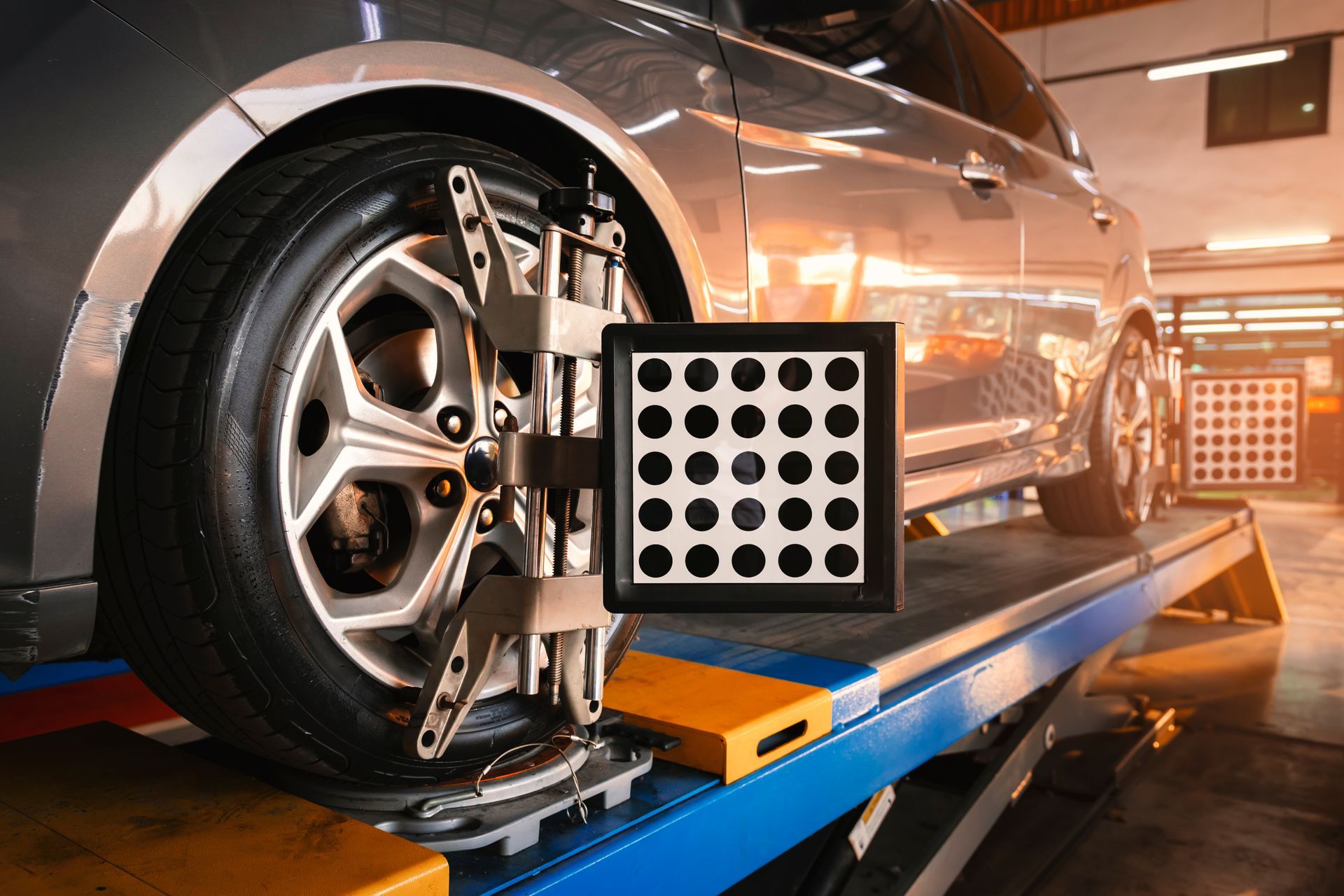 Car on a lift undergoing wheel alignment; sensor attached to wheel, targeting board in front.