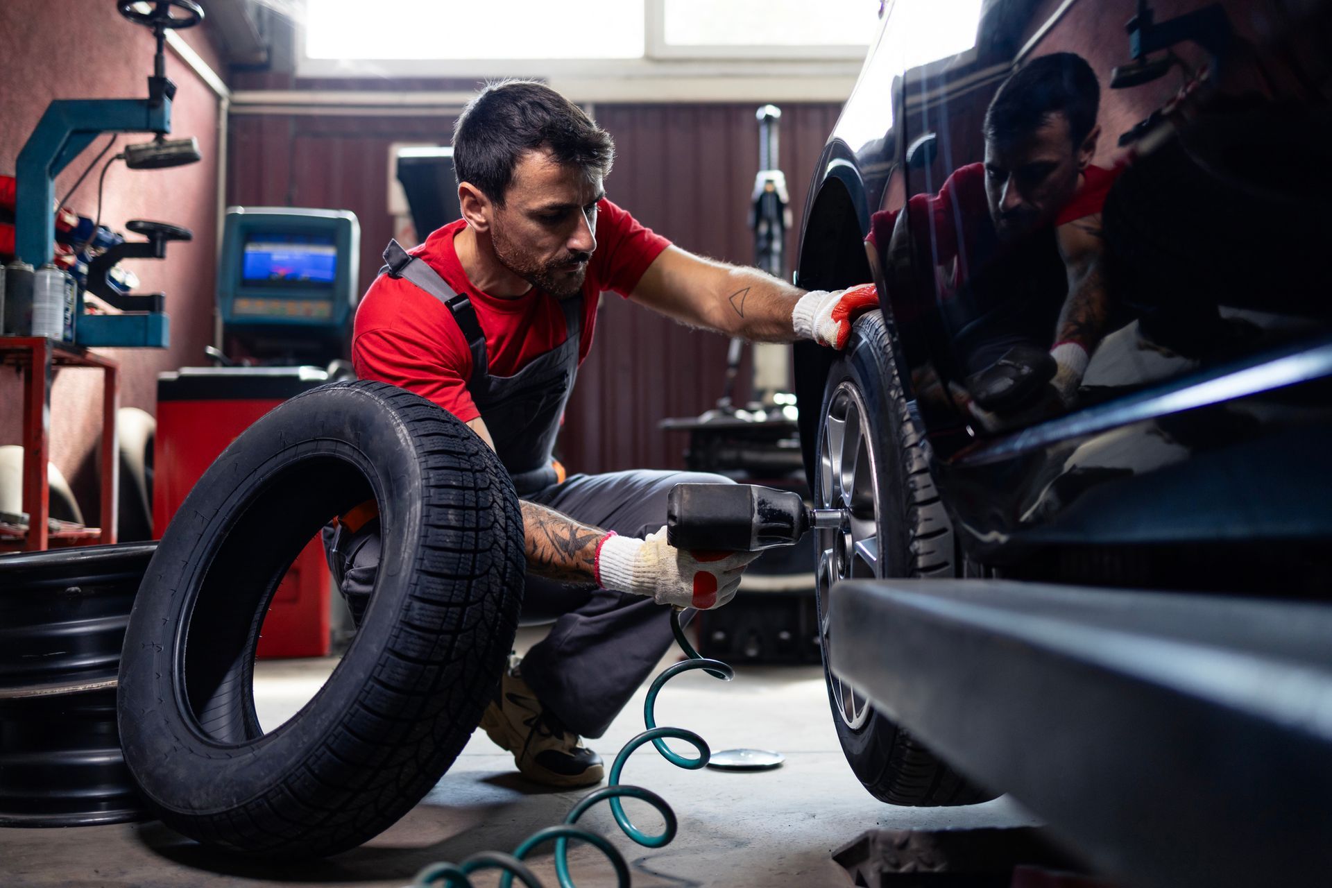 Mechanic changing a tire in a garage. He is using a power tool on the wheel.