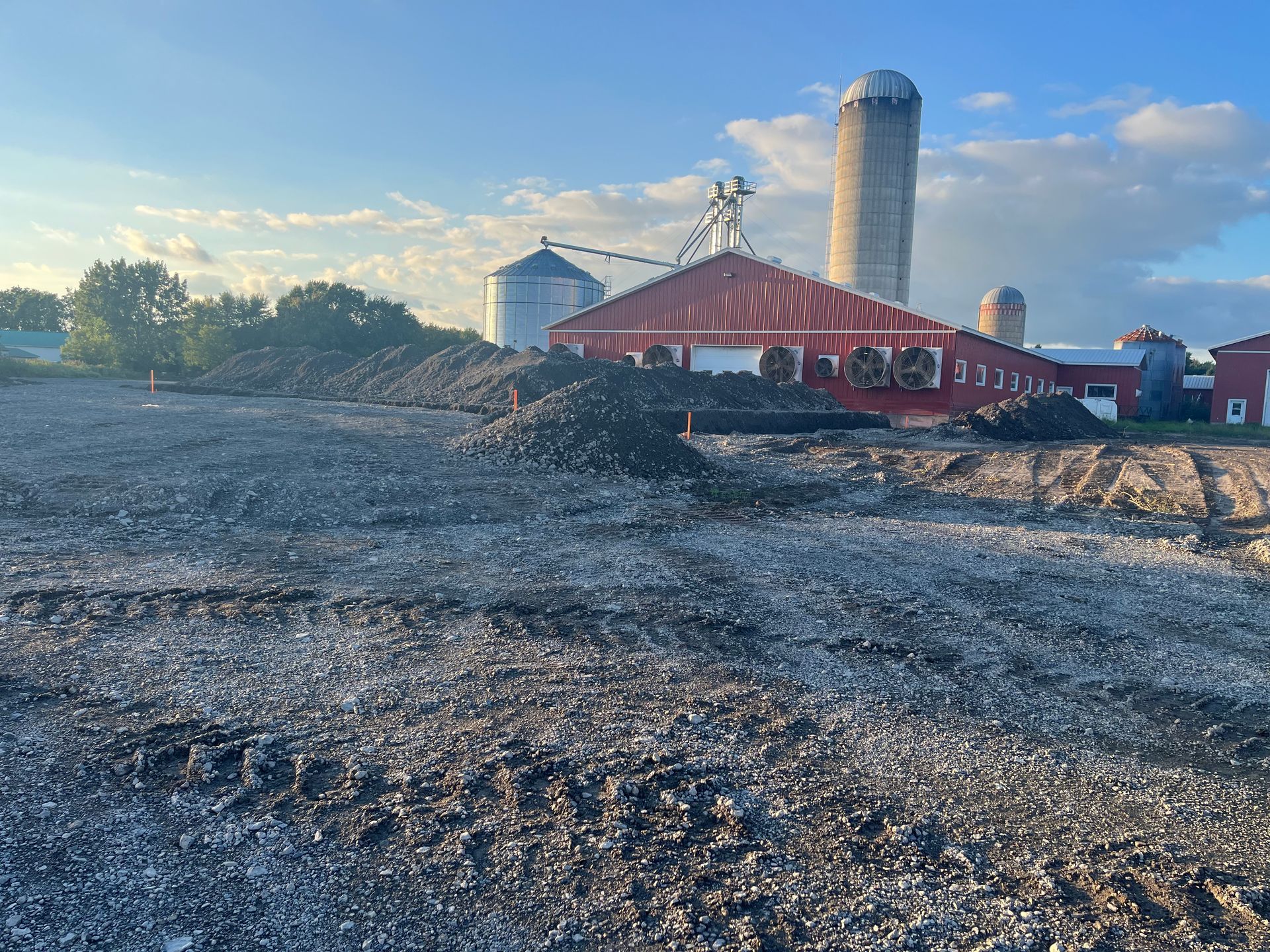 Paysage agricole avec silos, grange rouge et tas de matériaux sombres. Ciel bleu en arrière-plan.