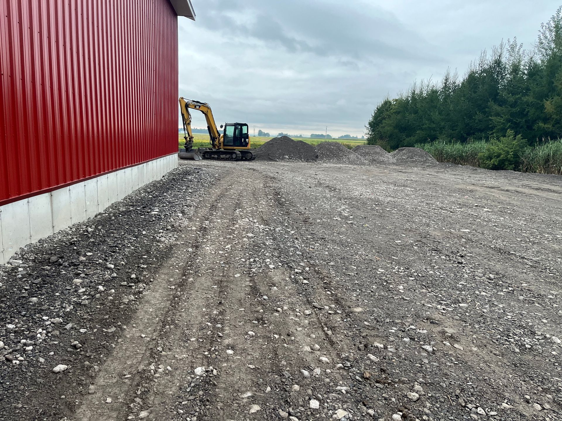 Chantier de construction avec un bâtiment rouge, une excavatrice et un sol gravillonné.