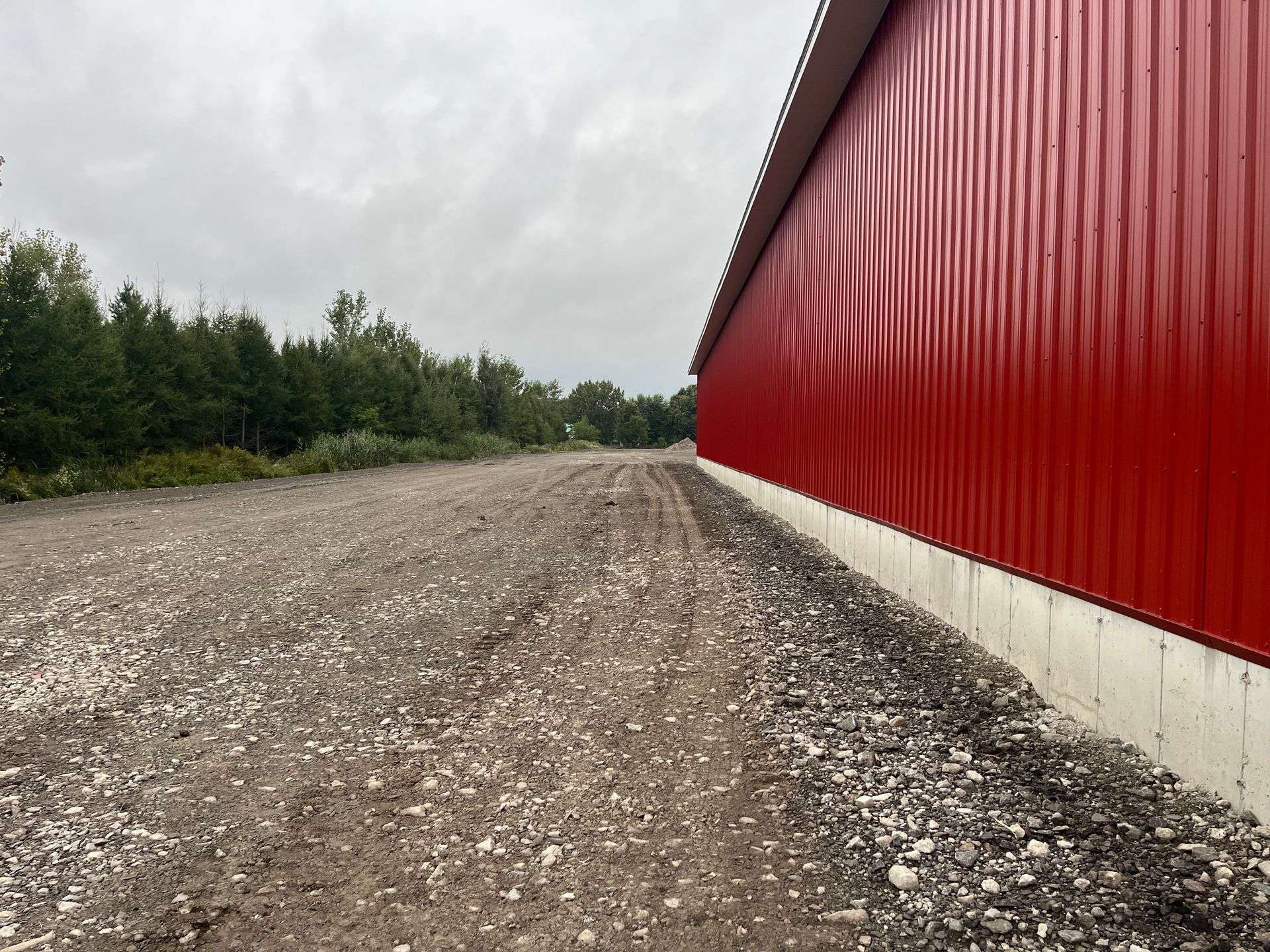 Bâtiment rouge bordé d'un chemin de gravier, arbres au loin sous un ciel couvert.