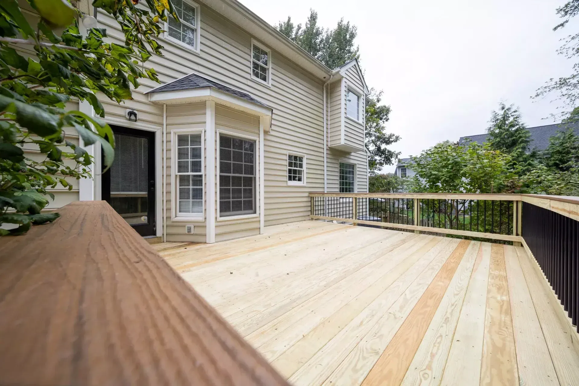 A freshly built wooden deck attached to the back of a beige two-story house with black railings.
