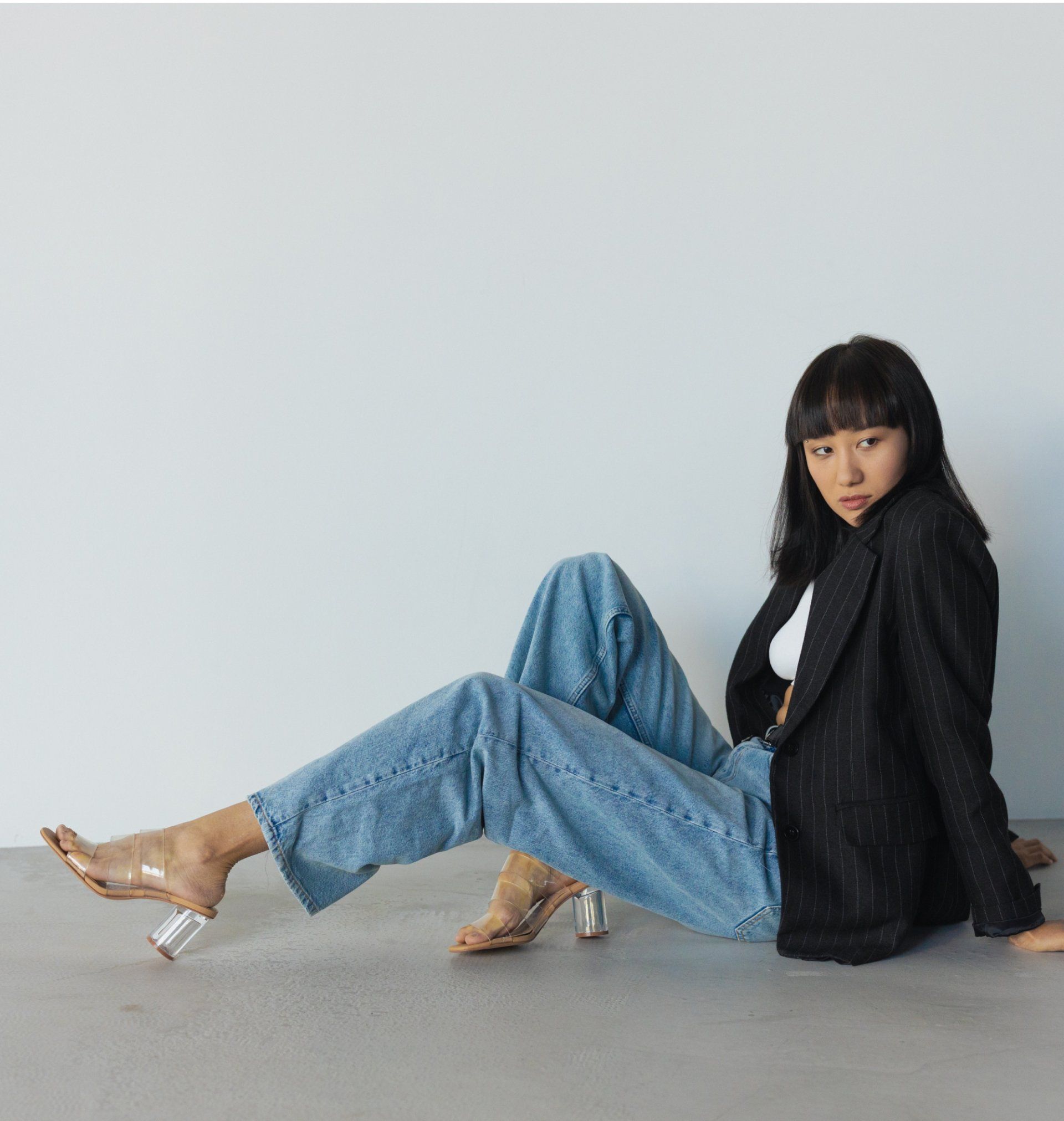 Woman wearing light wash denim jeans, black blazer, and clear heels.