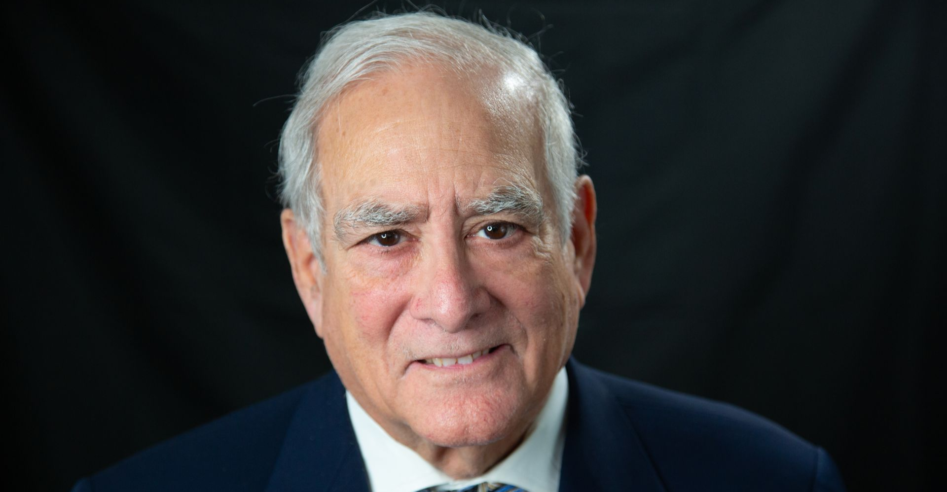 A woman is sitting at a desk with her hands folded and smiling.