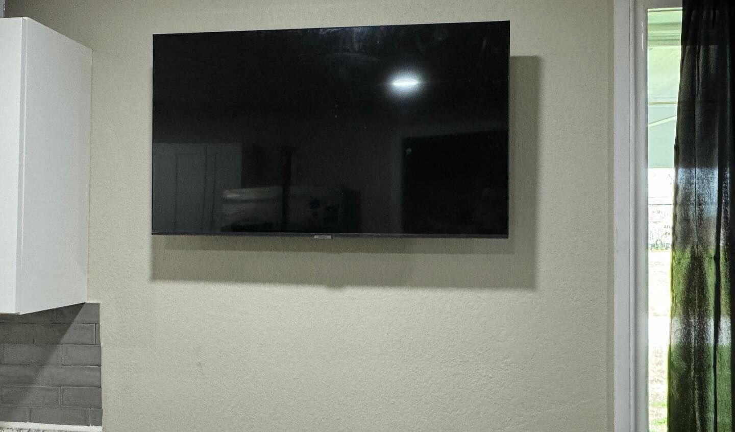 A flat screen tv is mounted on a wall next to a window.