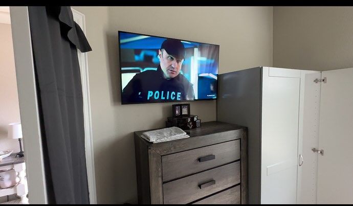 A bedroom with a dresser and a flat screen tv on the wall.
