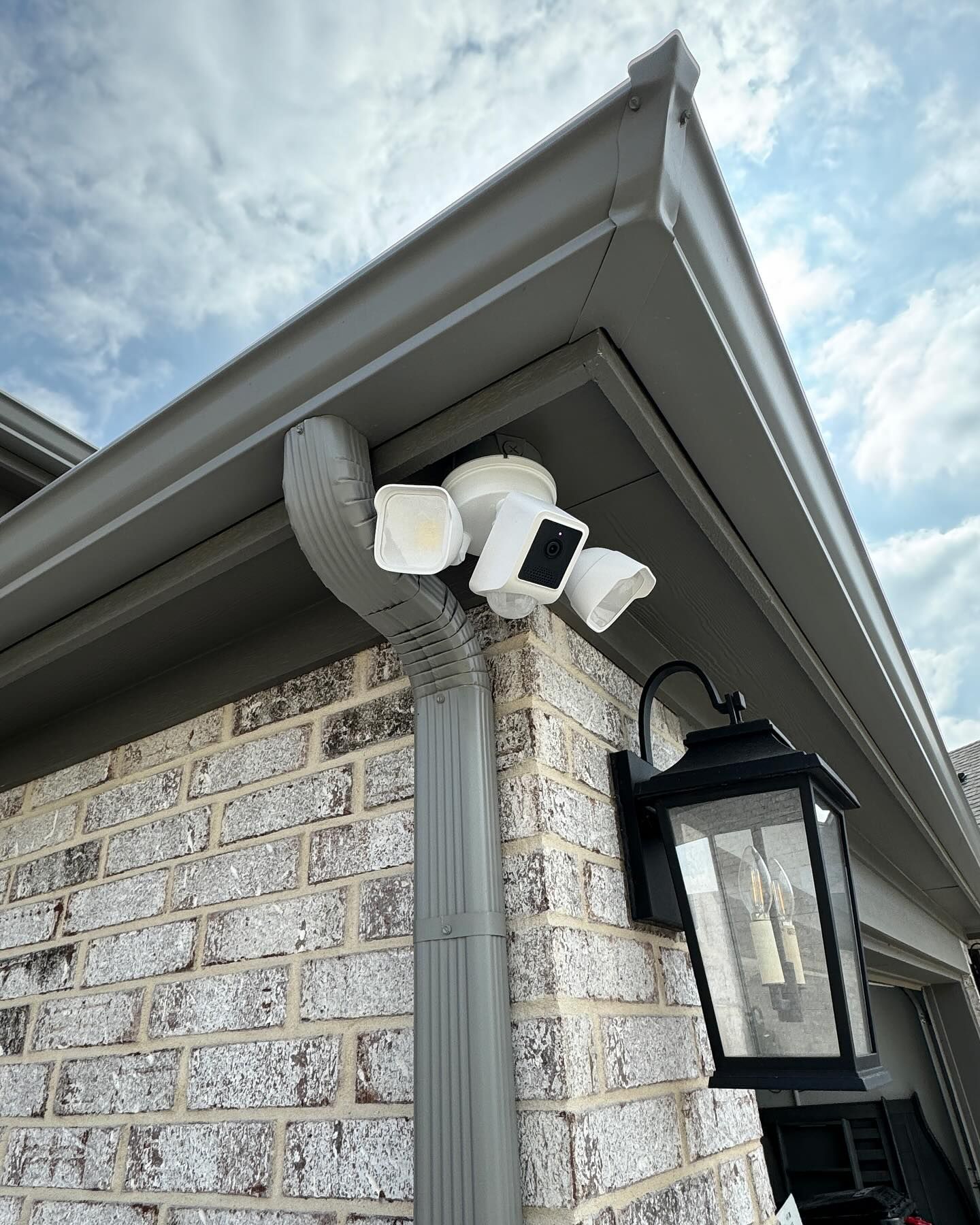 A security camera is mounted on the side of a brick house.