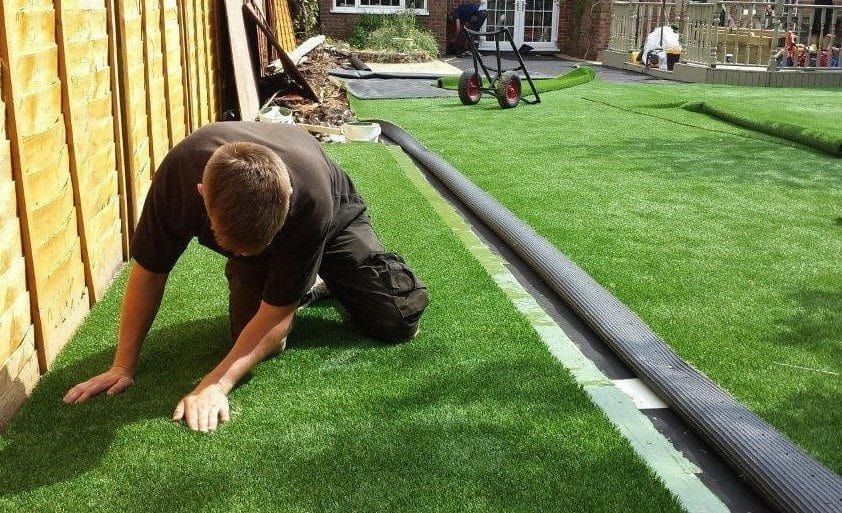 A Man Is Installing Artificial Grass in A Backyard — D-Scapes Landscaping Services Pty Ltd in Hallidays Point, NSW