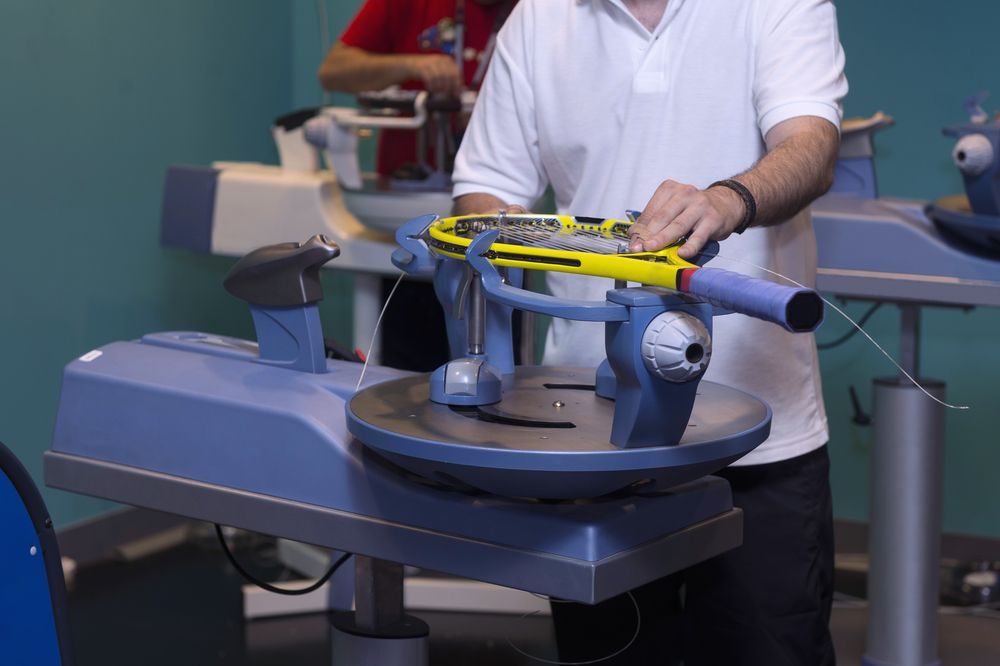 Man Stringing a Yellow Tennis Racket on a Blue Machine in a Well-lit Room — Topspin Tennis Newcastle in Lambton, NSW