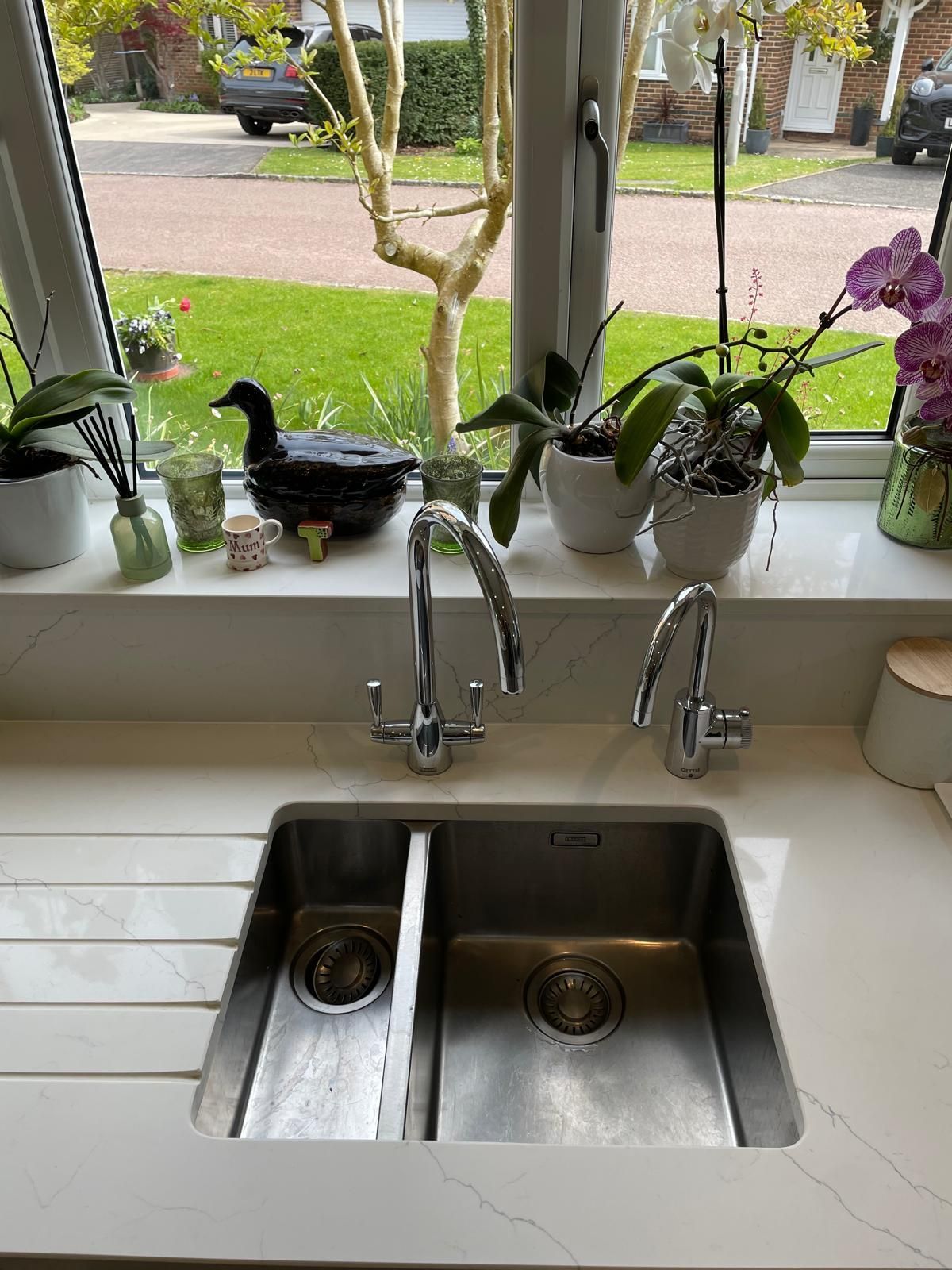 Kitchen sink beneath a window with potted plants on the sill and a street view outside.