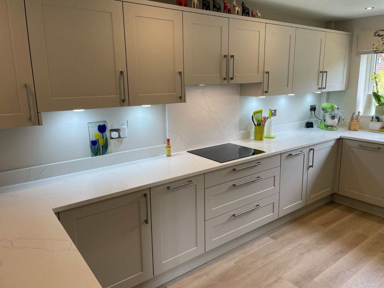 Modern beige kitchen with long countertop, built-in cabinets, sink, and wood flooring