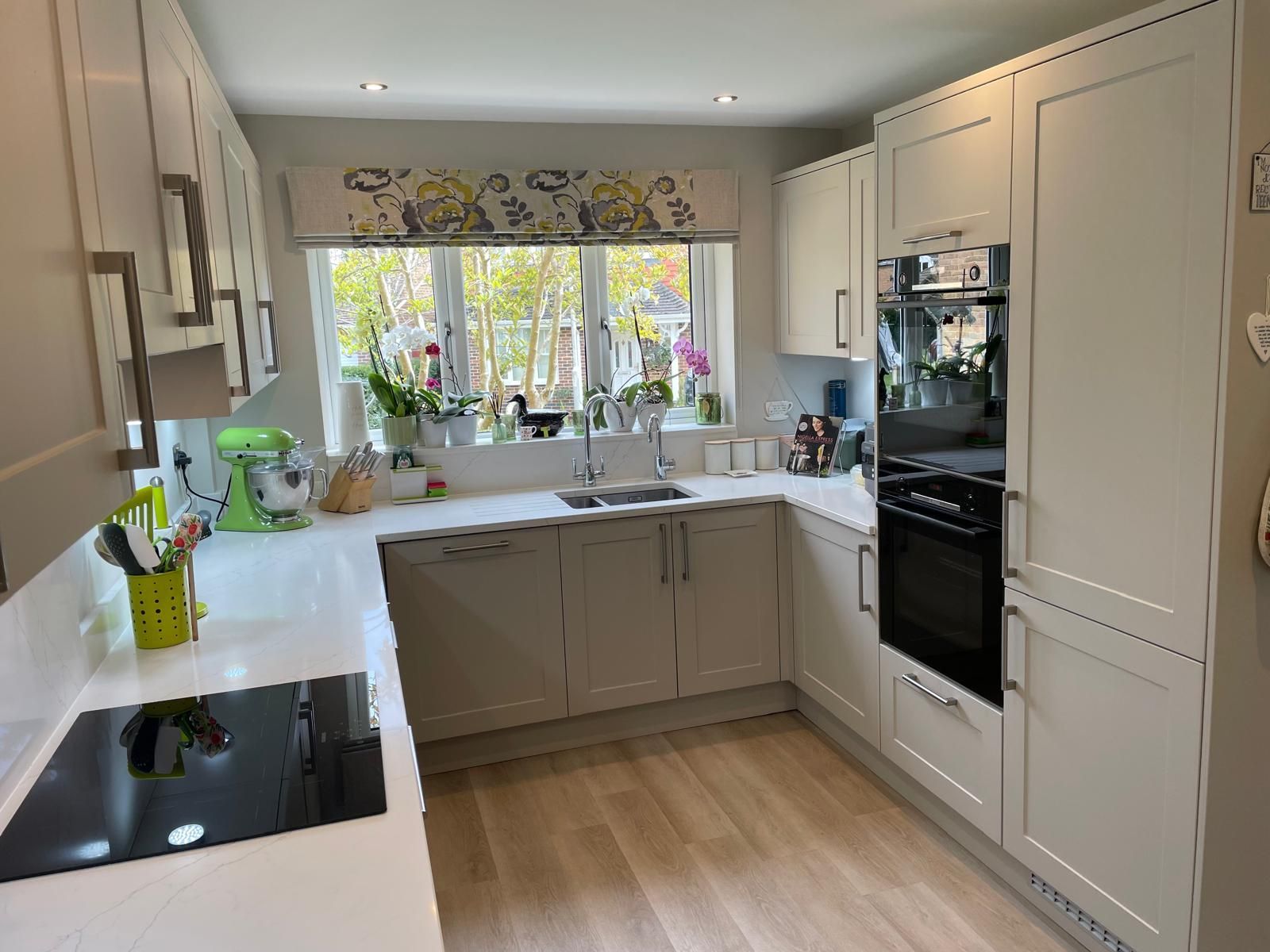 Bright modern kitchen with white cabinets, wood floor, and a window over a sink with flowers and greenery.