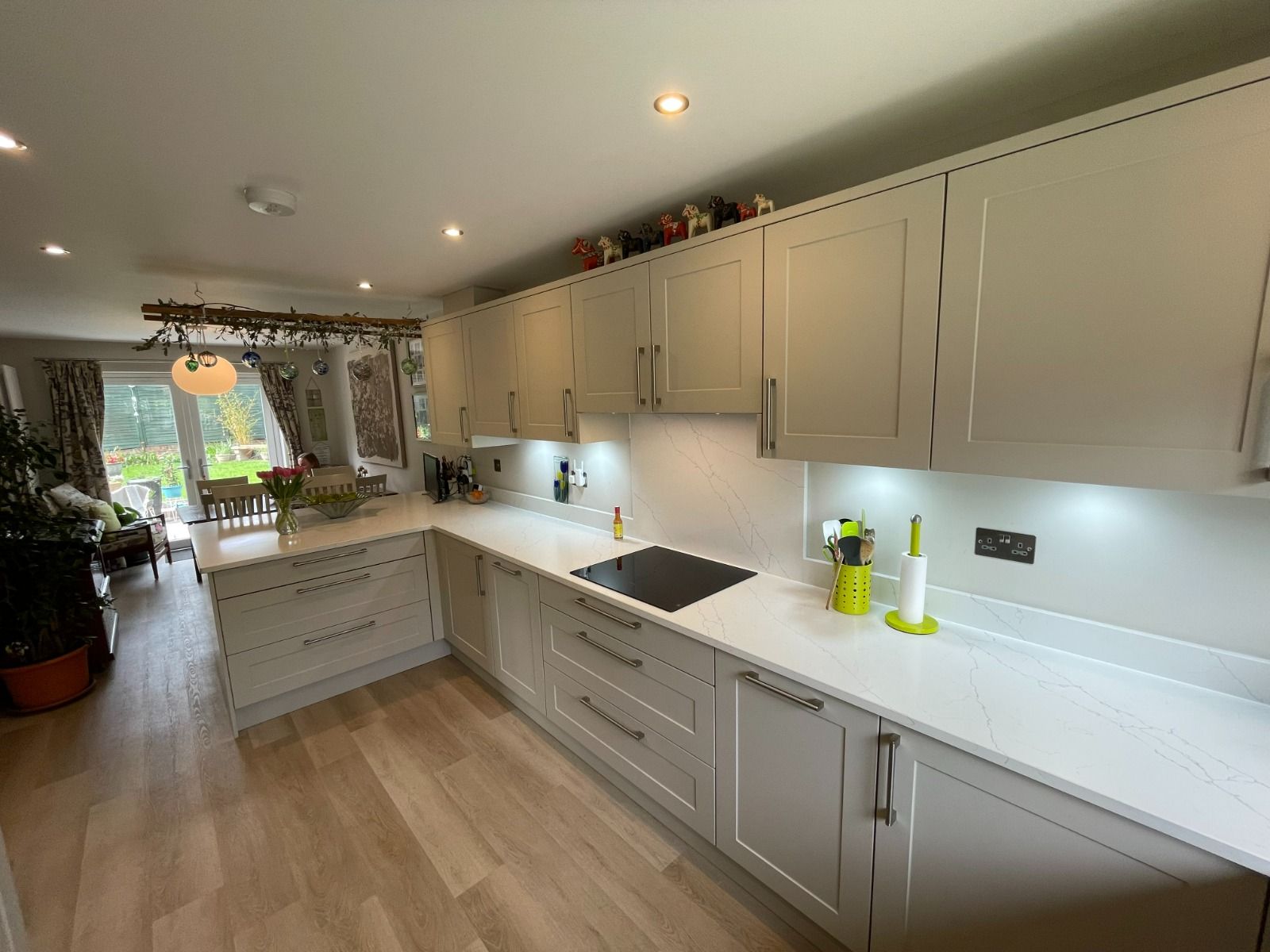 Bright modern kitchen with cream cabinets, white countertops, and light wood flooring; garden visible through back door