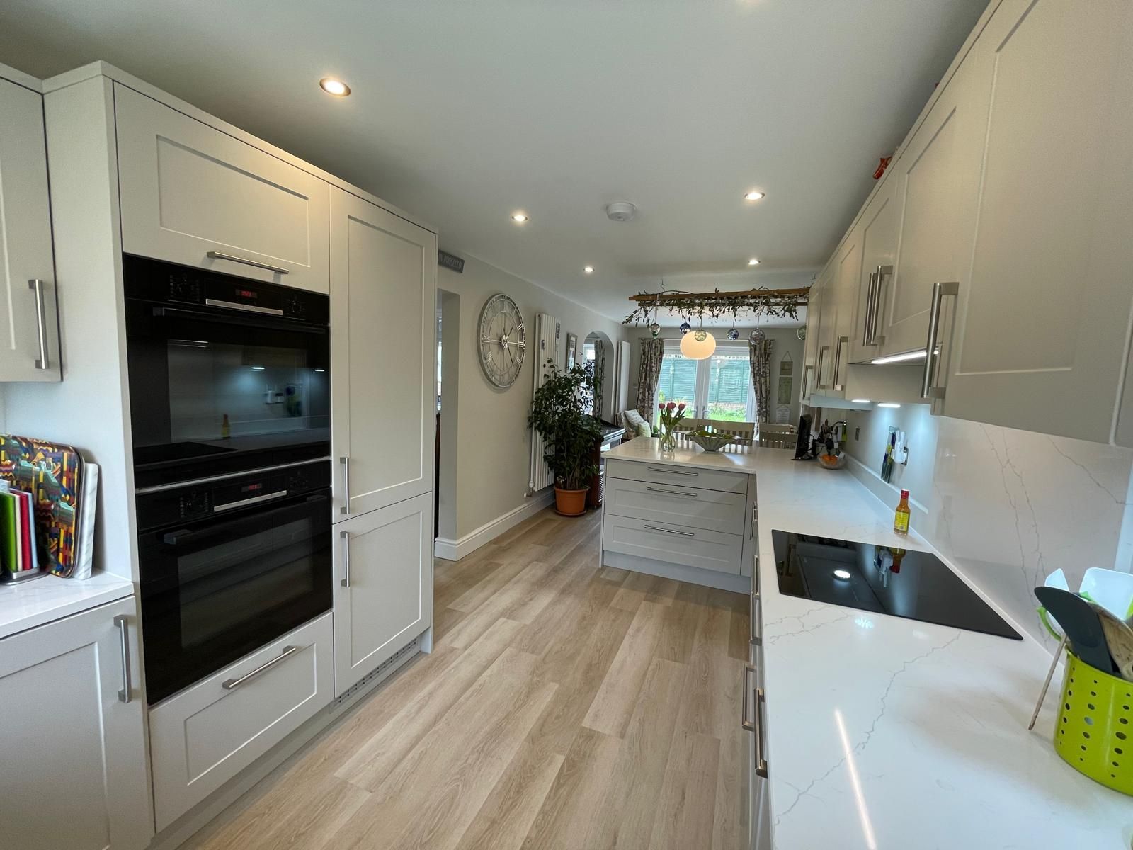 Bright modern white galley kitchen with built-in ovens, skylights, and wood flooring
