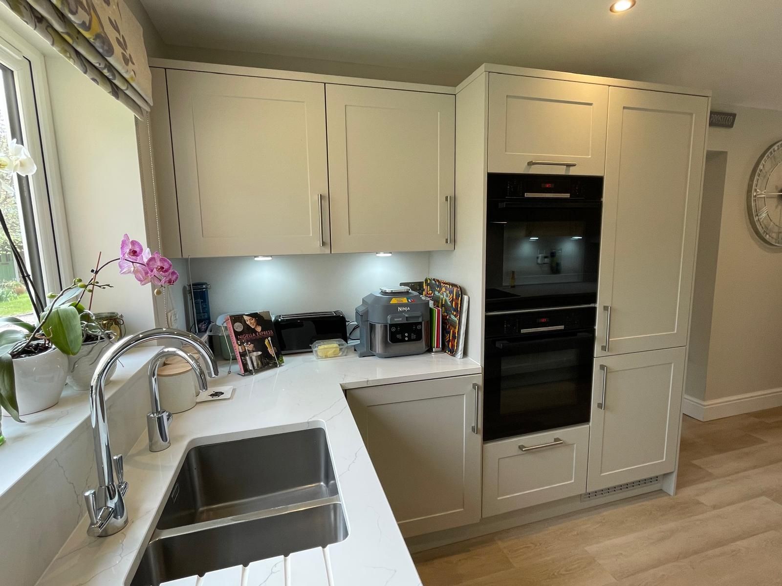 Bright white kitchen with stainless sink, built-in oven, countertop appliances, and a small orchid by the window