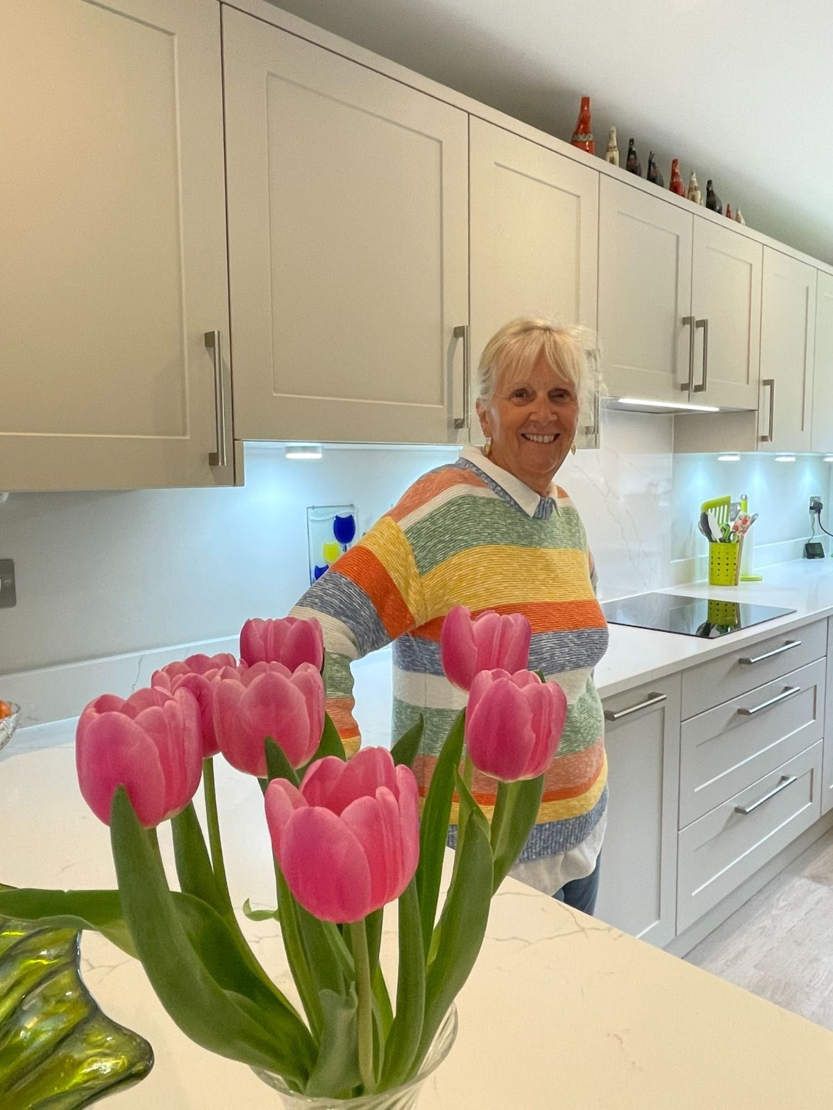 Woman in a white kitchen holding flowers, with pink tulips in the foreground.