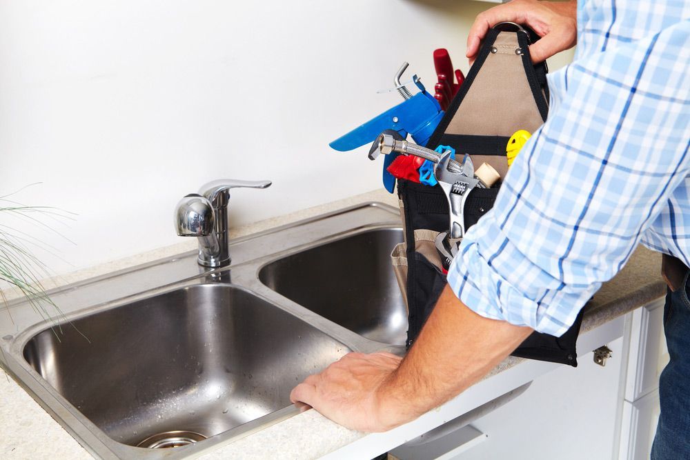 A Man Is Fixing A Kitchen Sink With A Tool Bag Full Of Tools — Tim Larkin Plumbing and Excavations in Laurieton, NSW
