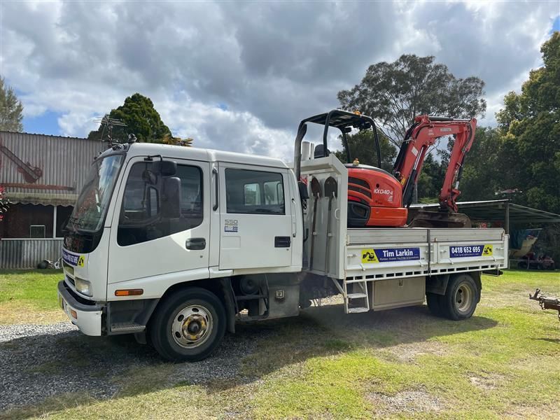 A Work Vehicle with an Excavator on the Back Tray — Tim Larkin Plumbing and Excavations in Laurieton, NSW