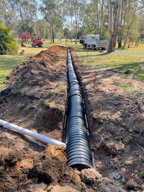 A Large Black Pipe Is Being Installed In The Dirt — Tim Larkin Plumbing and Excavations in Wauchope, NSW