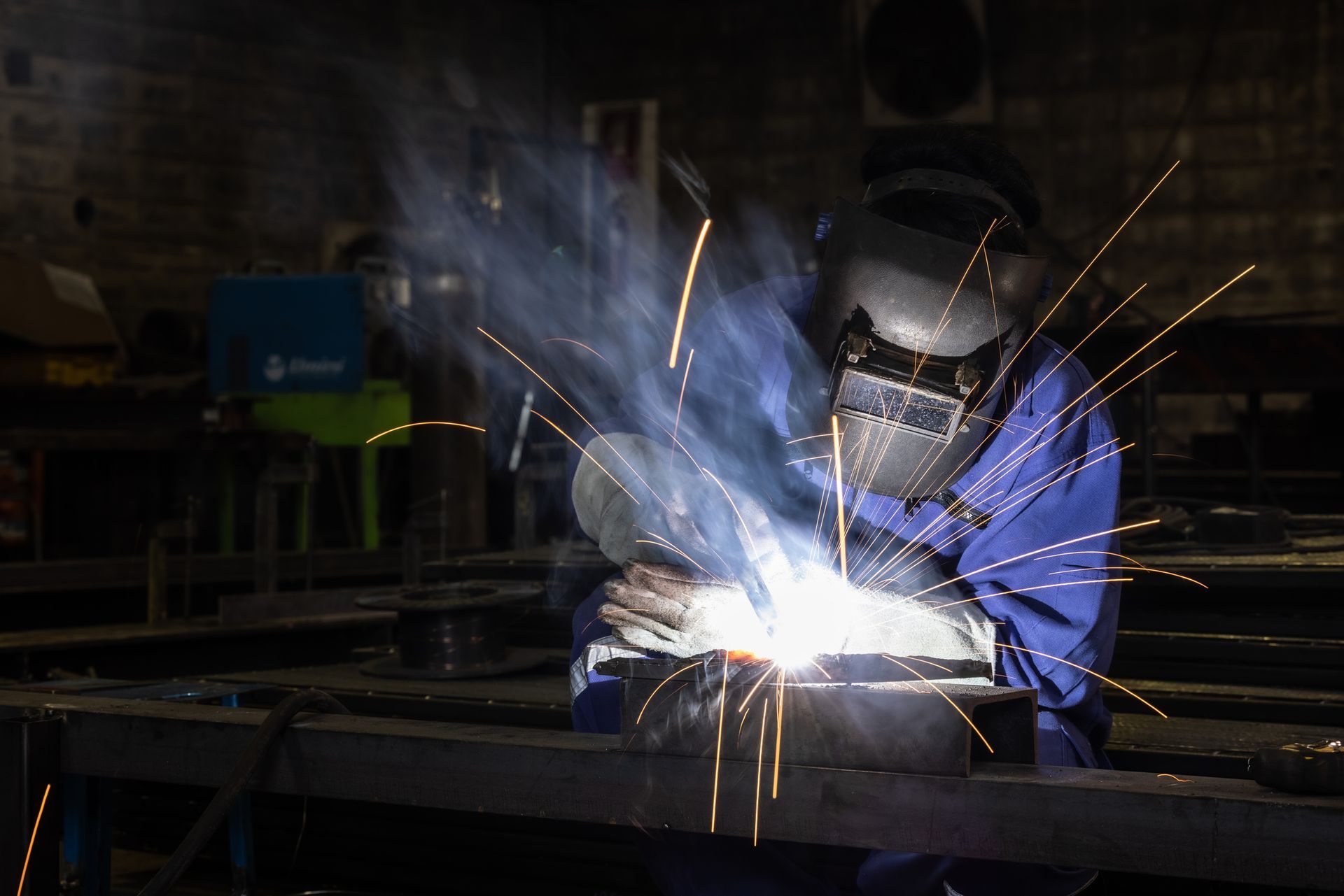 A man is welding a piece of metal in a dark room.