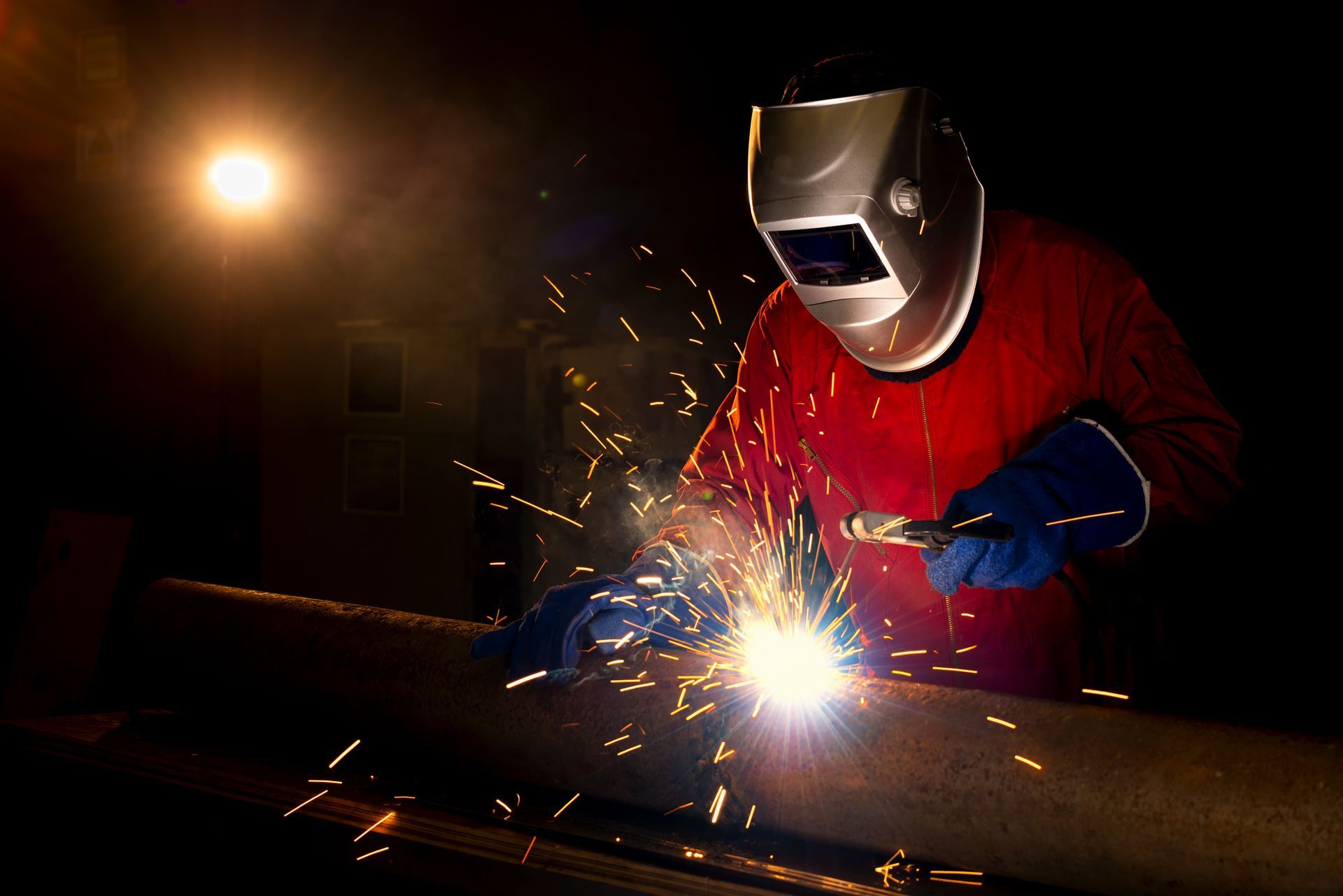 A man wearing a welding mask is welding a piece of metal