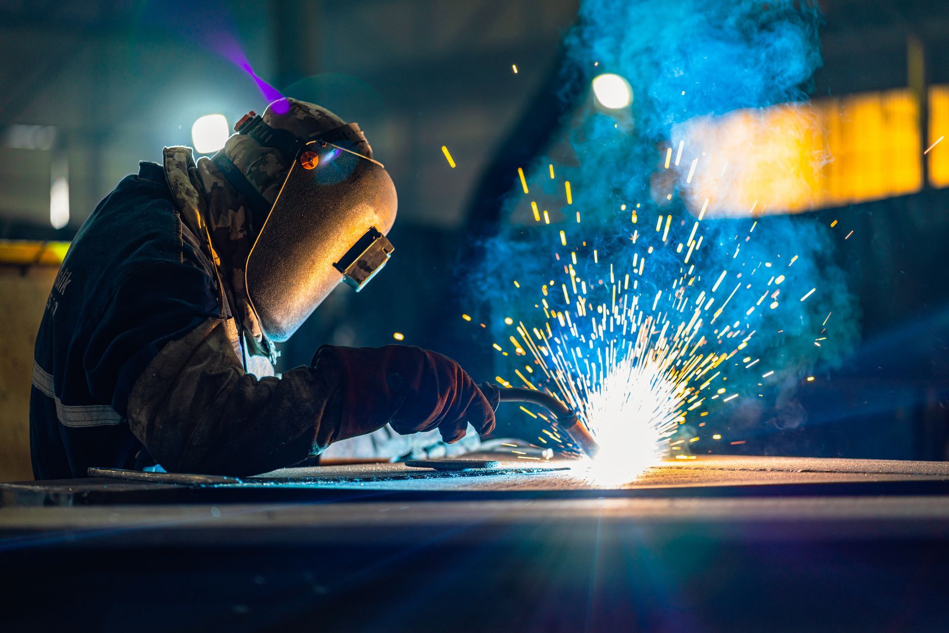 A man is welding a piece of metal in a factory.