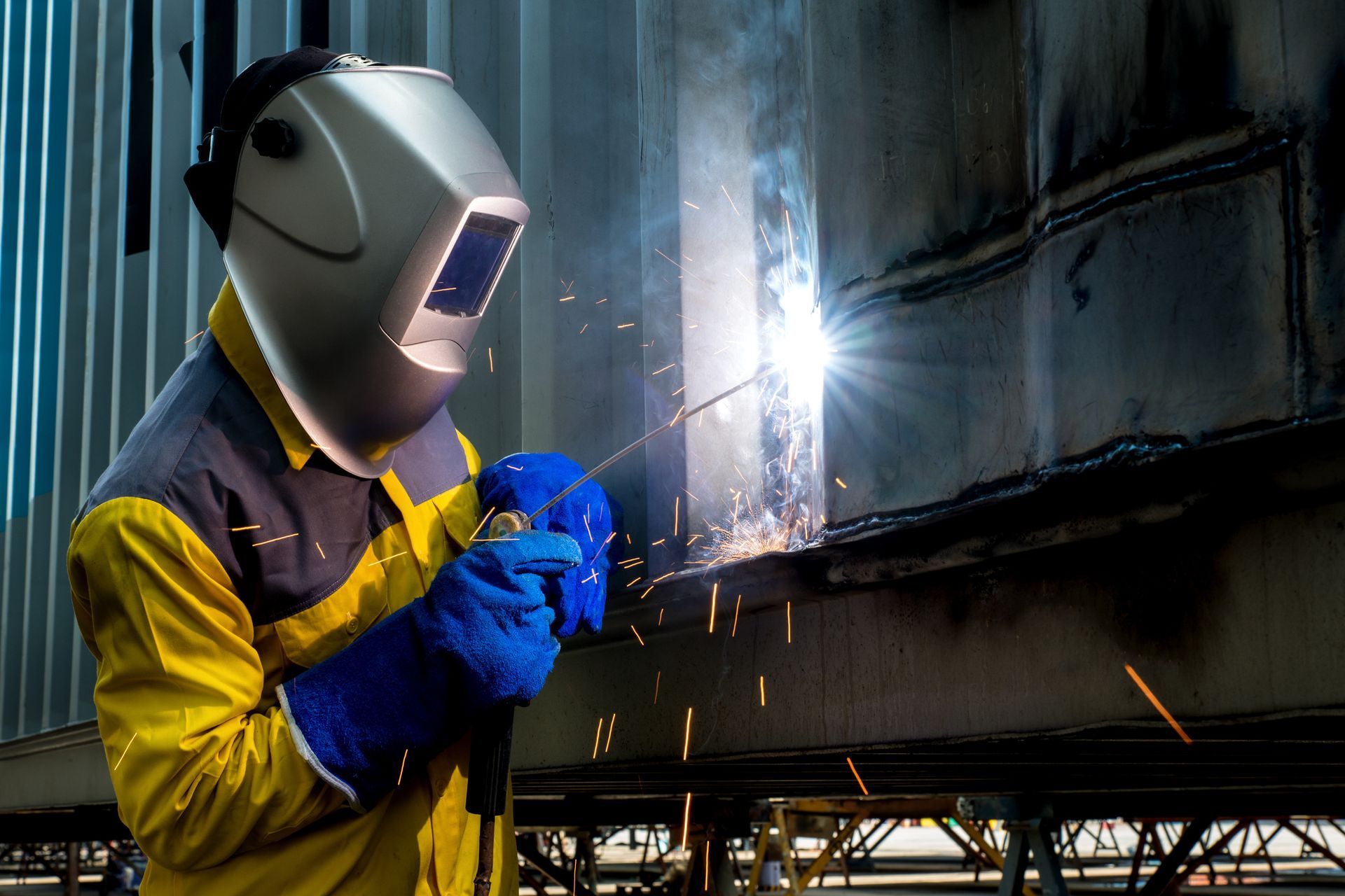 A man wearing a welding helmet is welding a piece of metal.