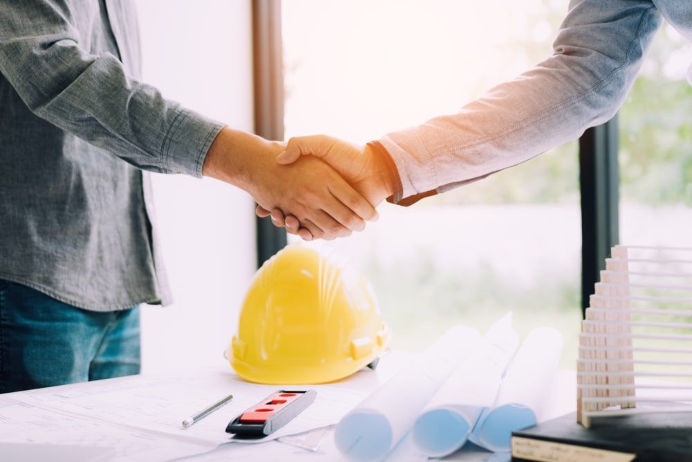 Two Men Shaking Hands Over A Table With A Hard Hat — Calibre Engineering In Mica Creak, QLD