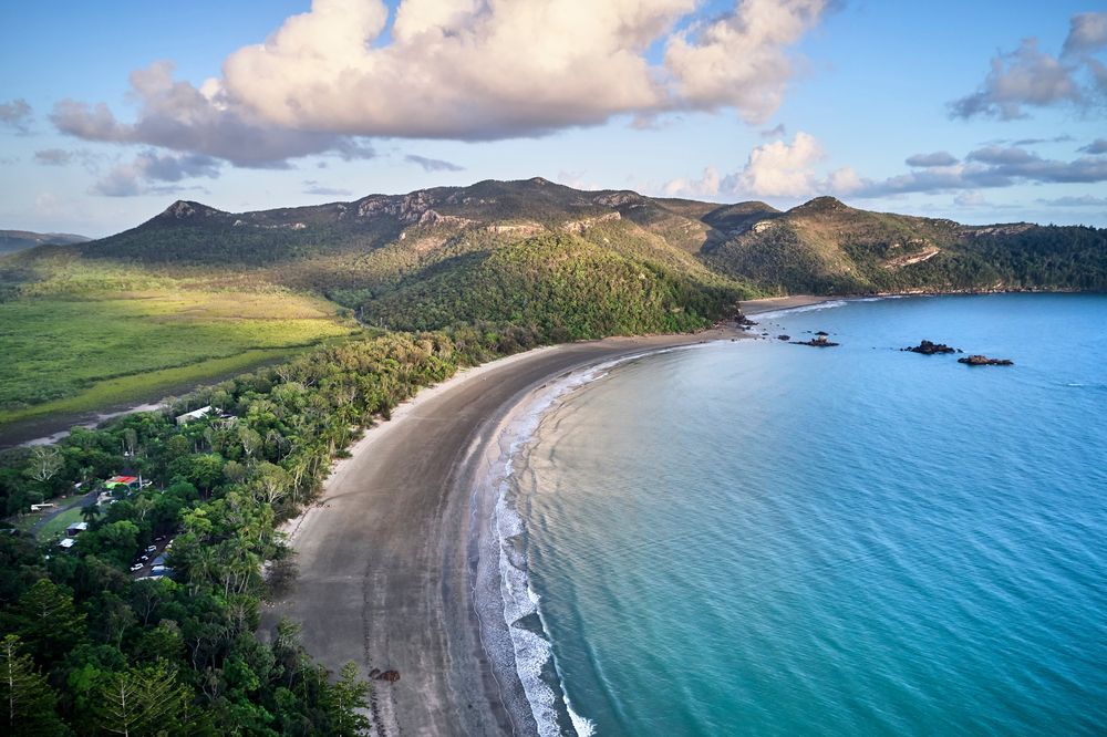 Aerial View Of A Beach With Mountains And A Body Of Water Surrounded By Trees — Calibre Engineering In Mackay, QLD
