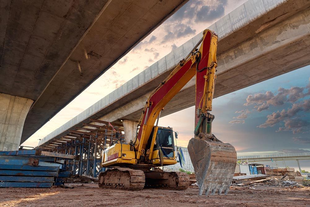 Yellow Excavator Working On A Construction Site Under A Bridge — Calibre Engineering In Mica Creak, QLD