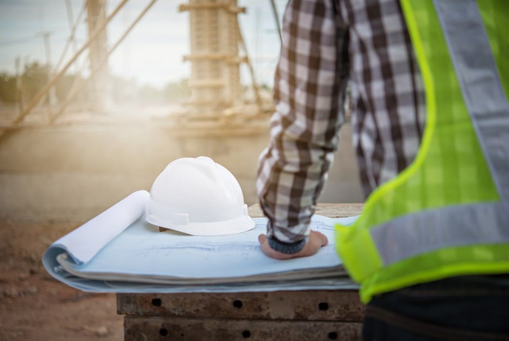 Construction Worker Standing Next To A Hard Hat And Blueprints At A Construction Site — Calibre Engineering In Mount Isa, QLD
