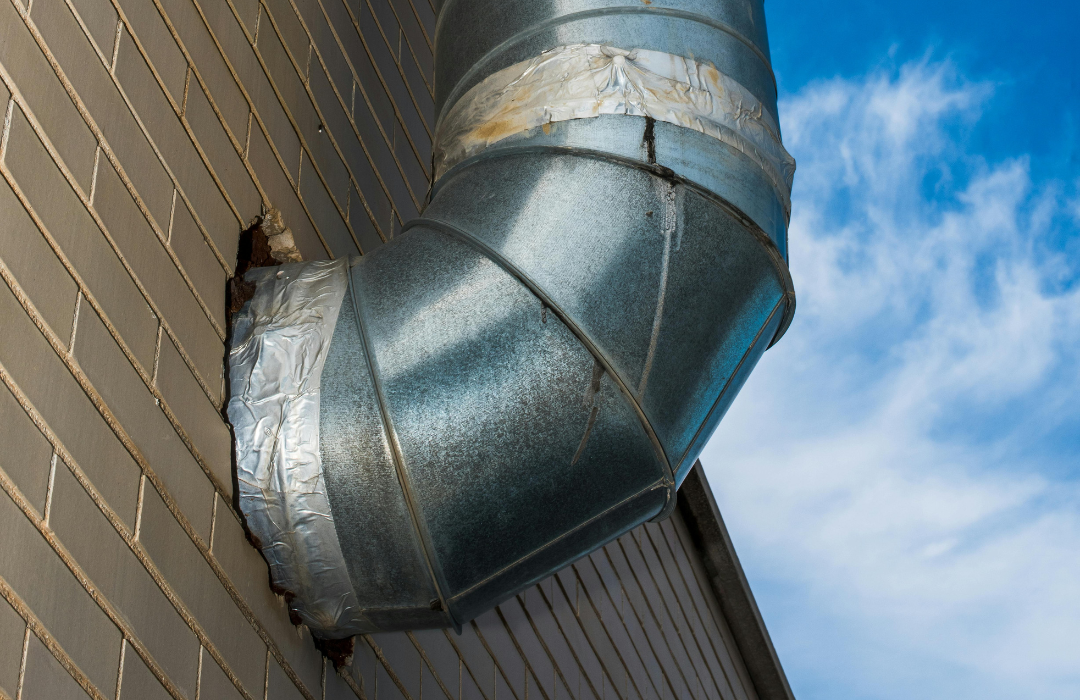 A metal pipe is attached to the side of a brick building.