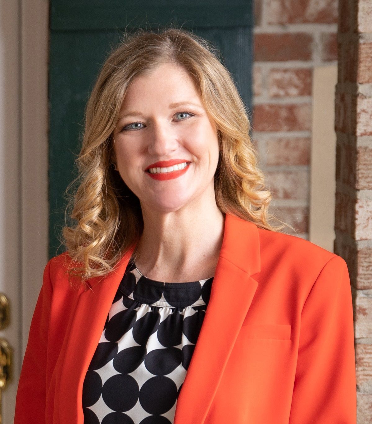 A woman wearing an orange jacket and polka dot dress is smiling for the camera.