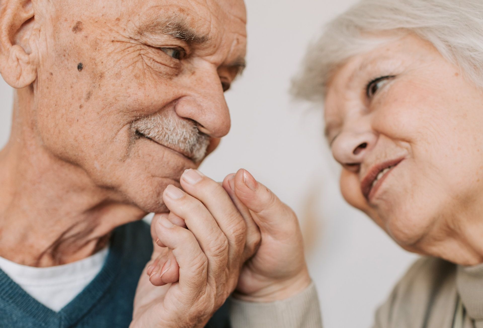 An elderly couple is holding hands and looking at each other.