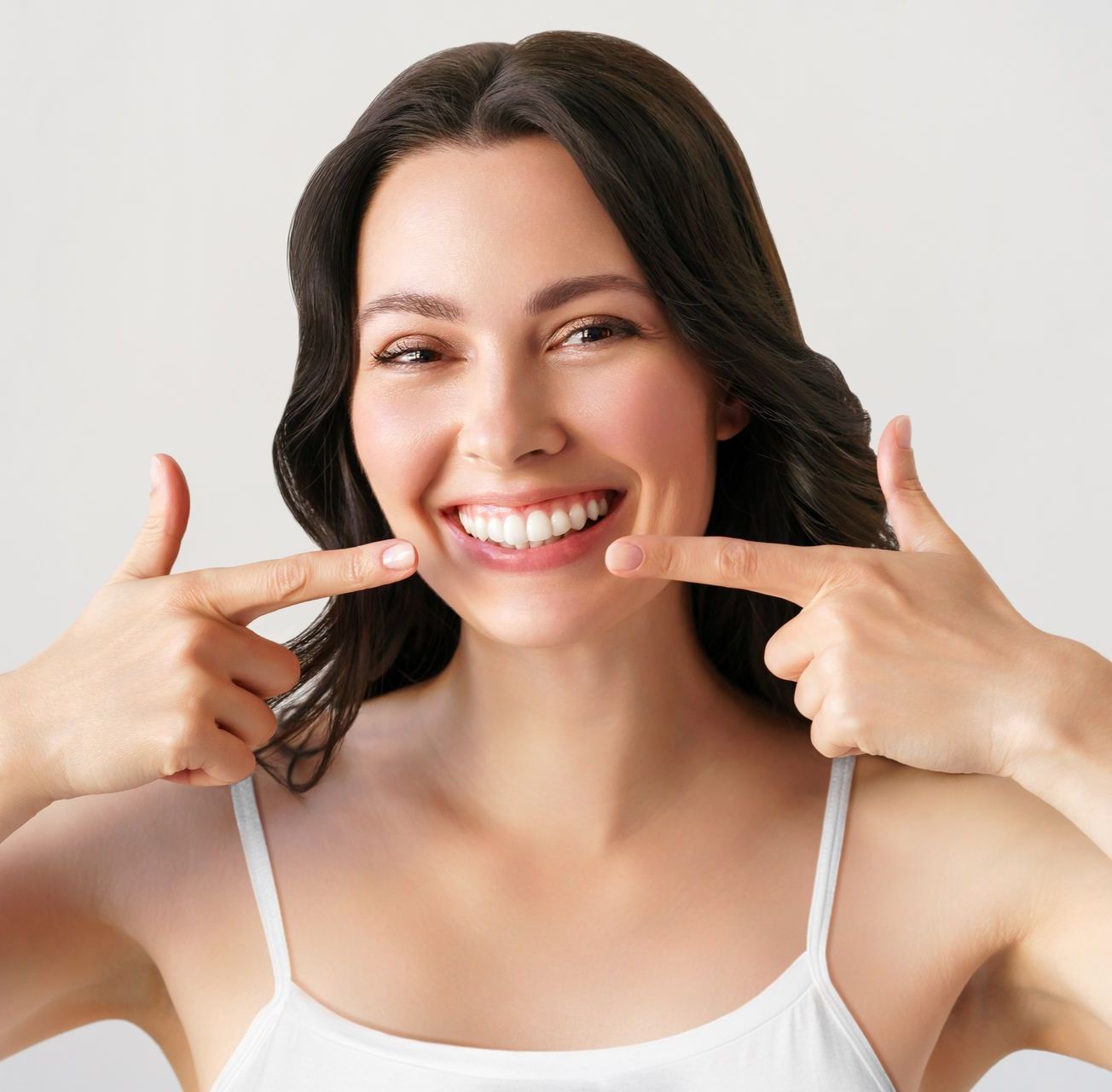 Una donna con una canottiera bianca sorride e indica i suoi denti. - Arte Dentale Frosinone