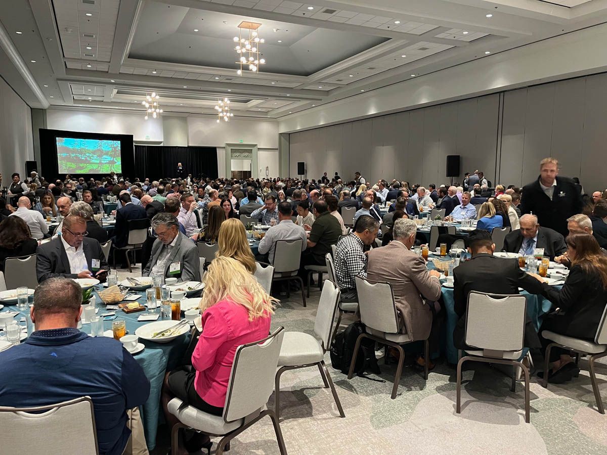 A large group of people are sitting at tables in a large room at a conference.