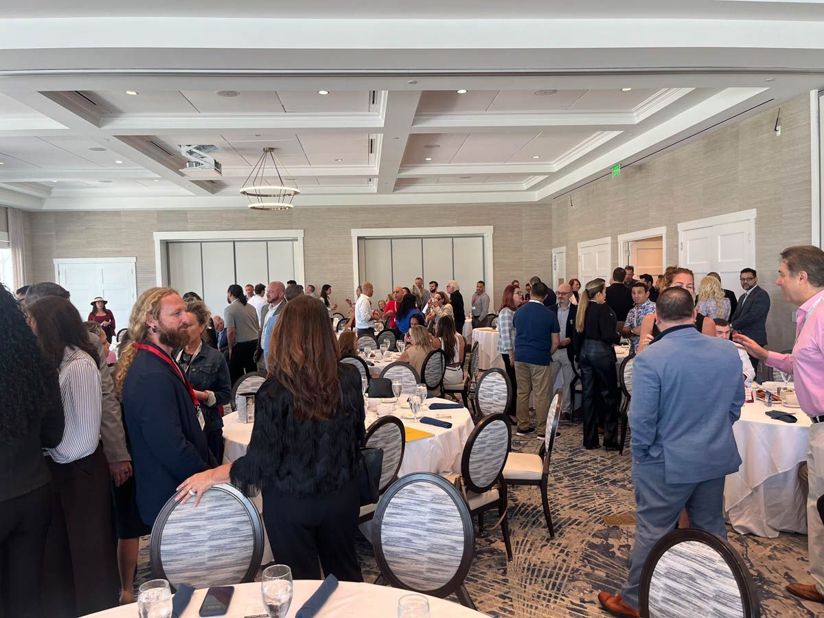 A large group of people are standing around tables in a large room.